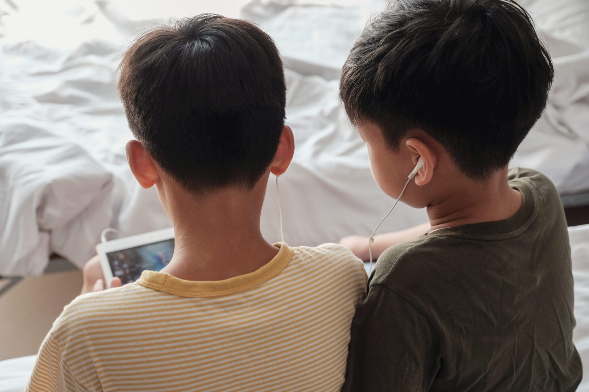 Tween boys using tablet and sharing earphones, listening to podcast, music, playing games, and using internet technology.